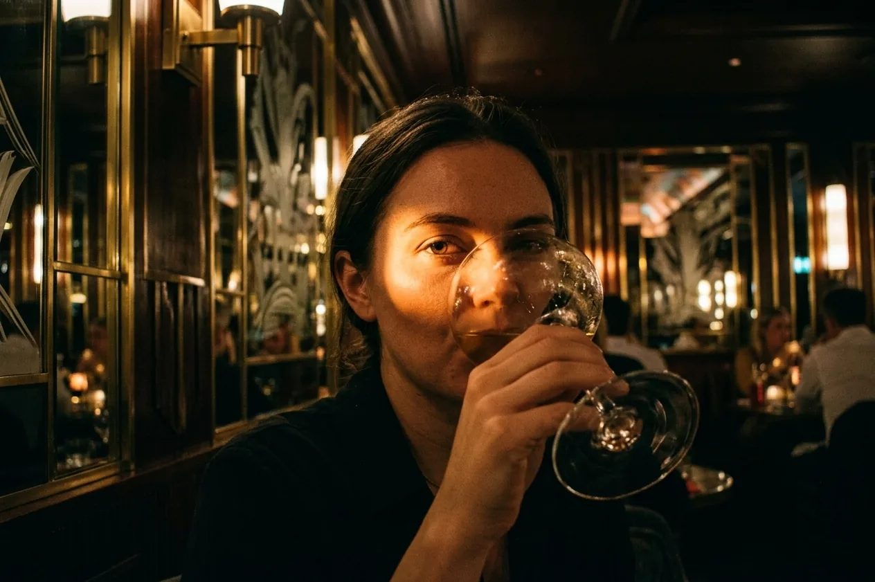 En gäst dricker vin, ansiktet halvskymt i det varma kvällsljuset.